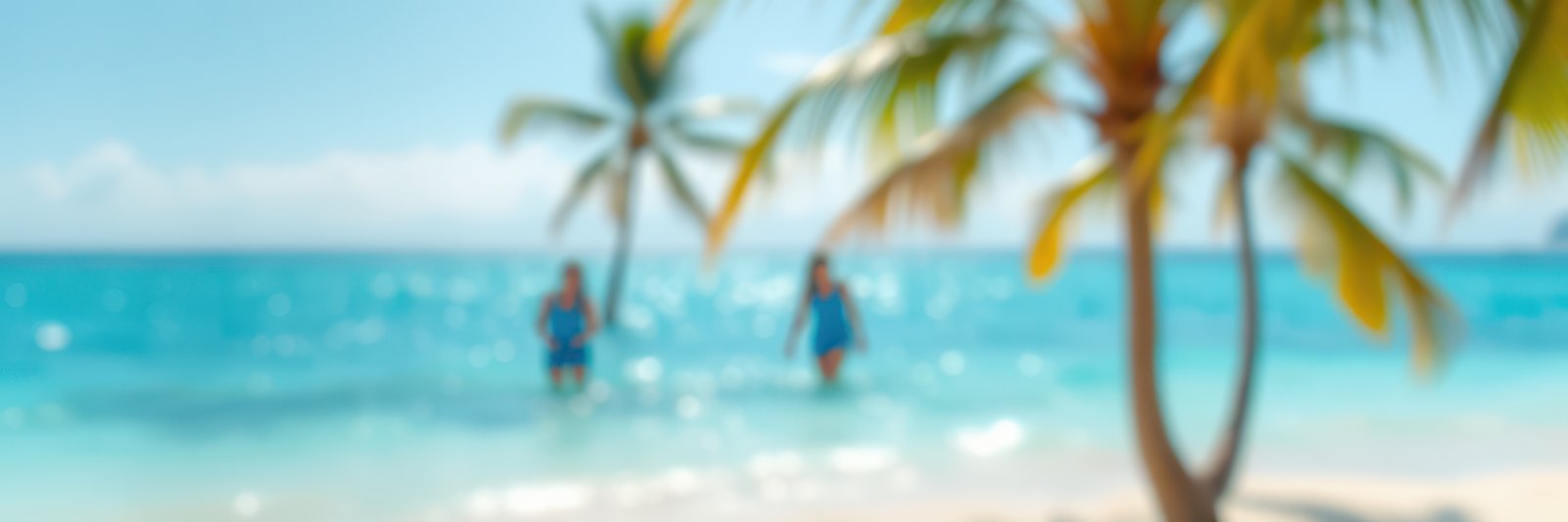 Two people walking in shallow turquoise water under clear skies near palm trees on a sunny beach in tropical paradise